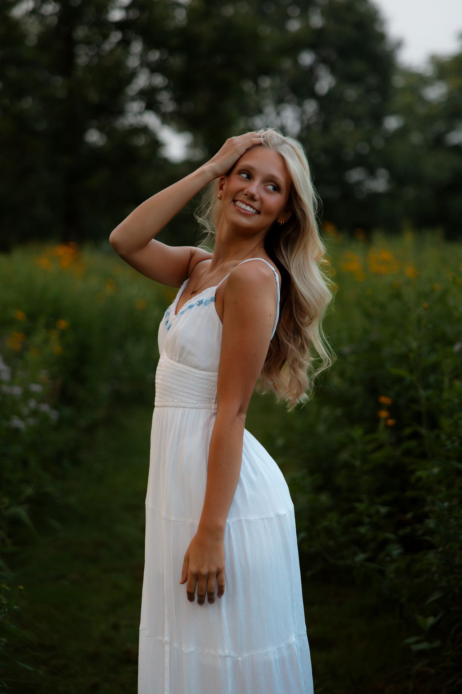 Portrait of a smiling young woman with blonde hair wearing a light blue off-shoulder top against a blue background.