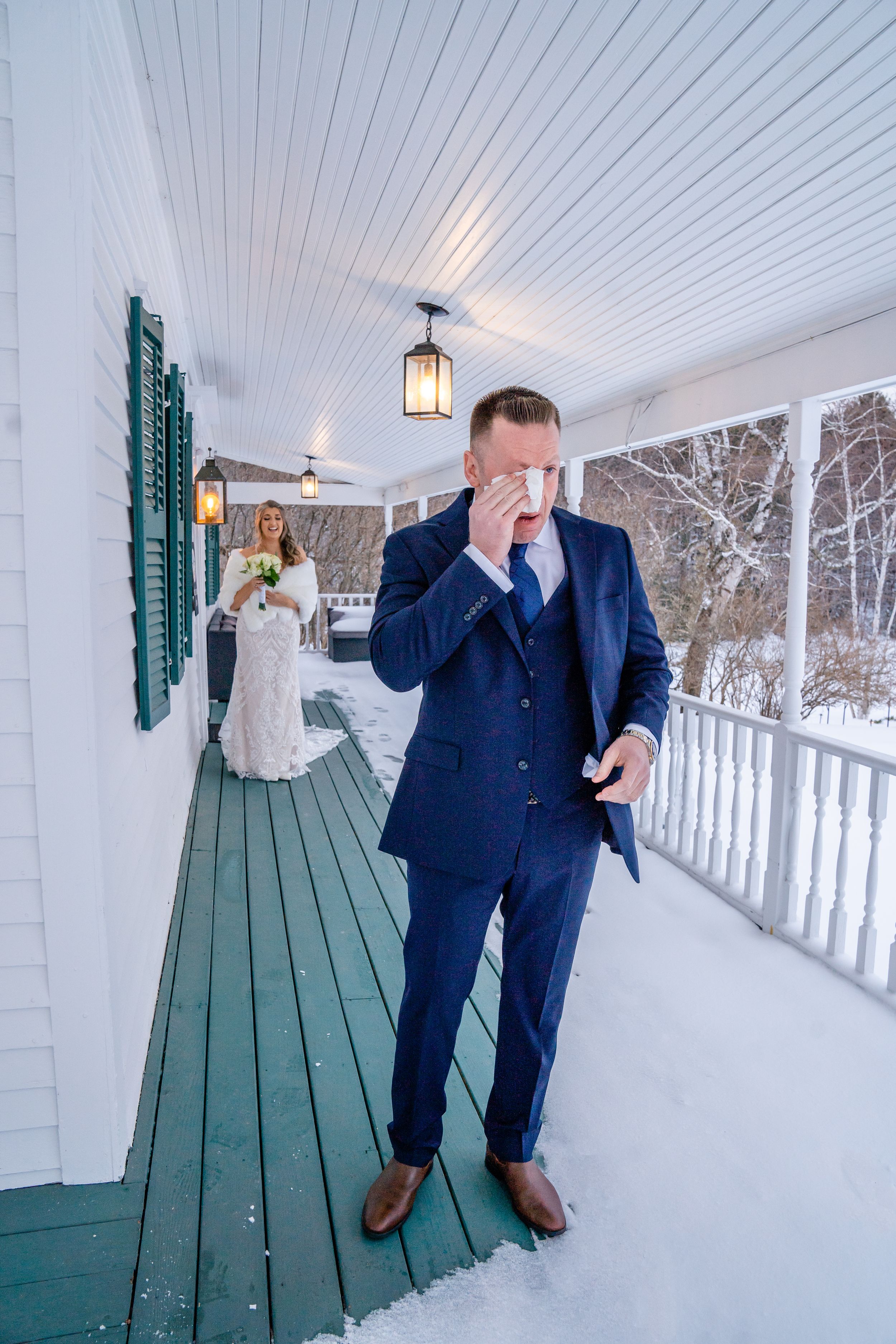 A winter wedding first look moment captured on a snowy white porch with green wooden floors and lantern lighting.