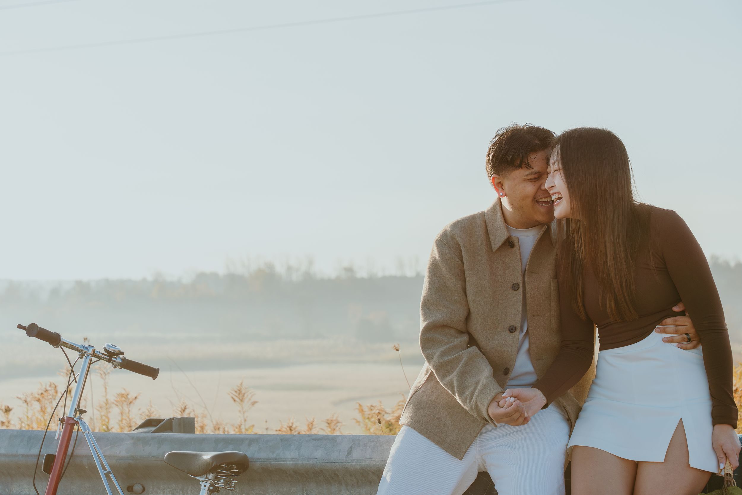 A romantic couple shares an intimate moment next to a bicycle on a scenic road at sunset.