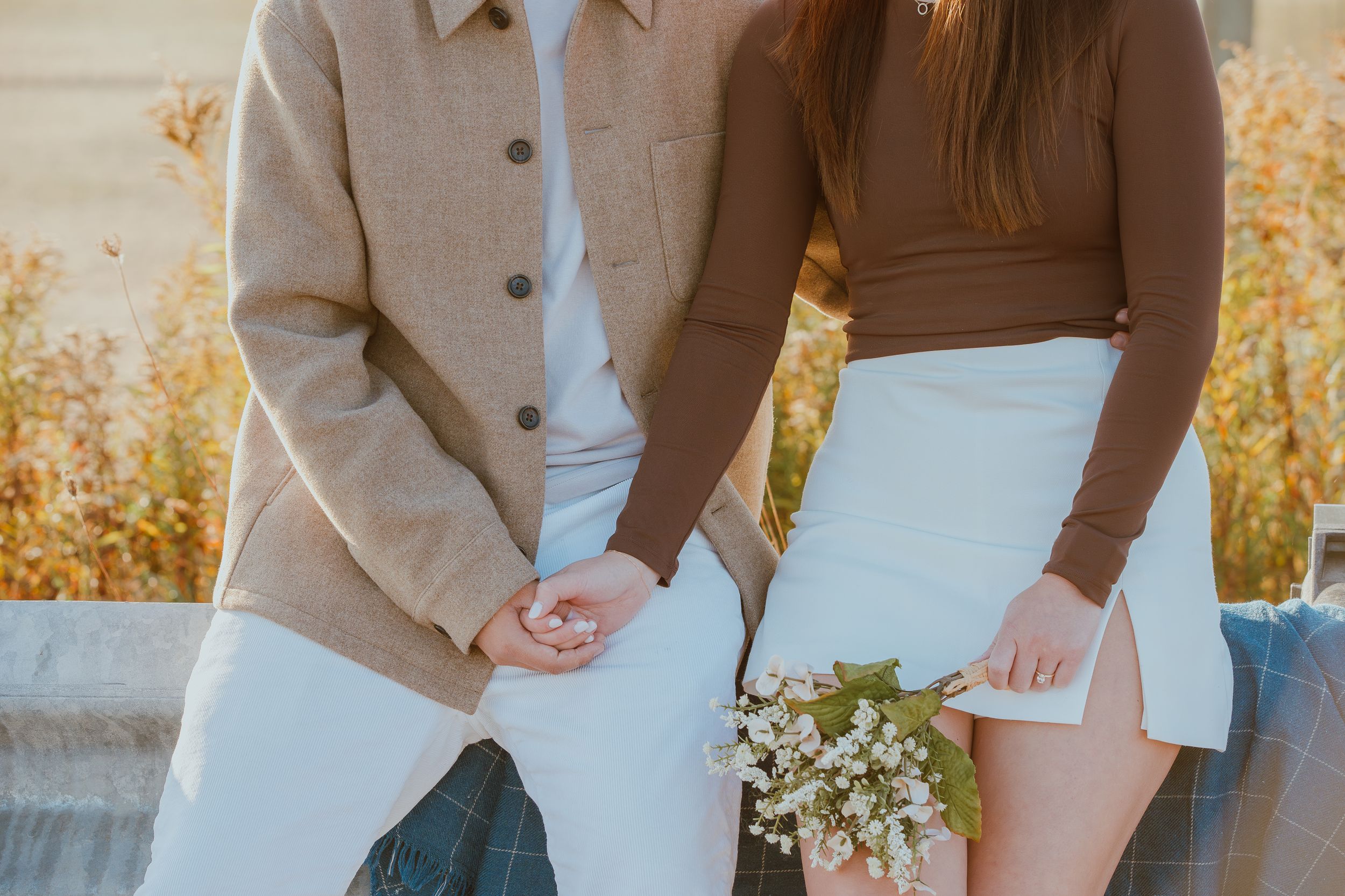 Couple in coordinated beige and white outfits holding small white flowers outdoors.