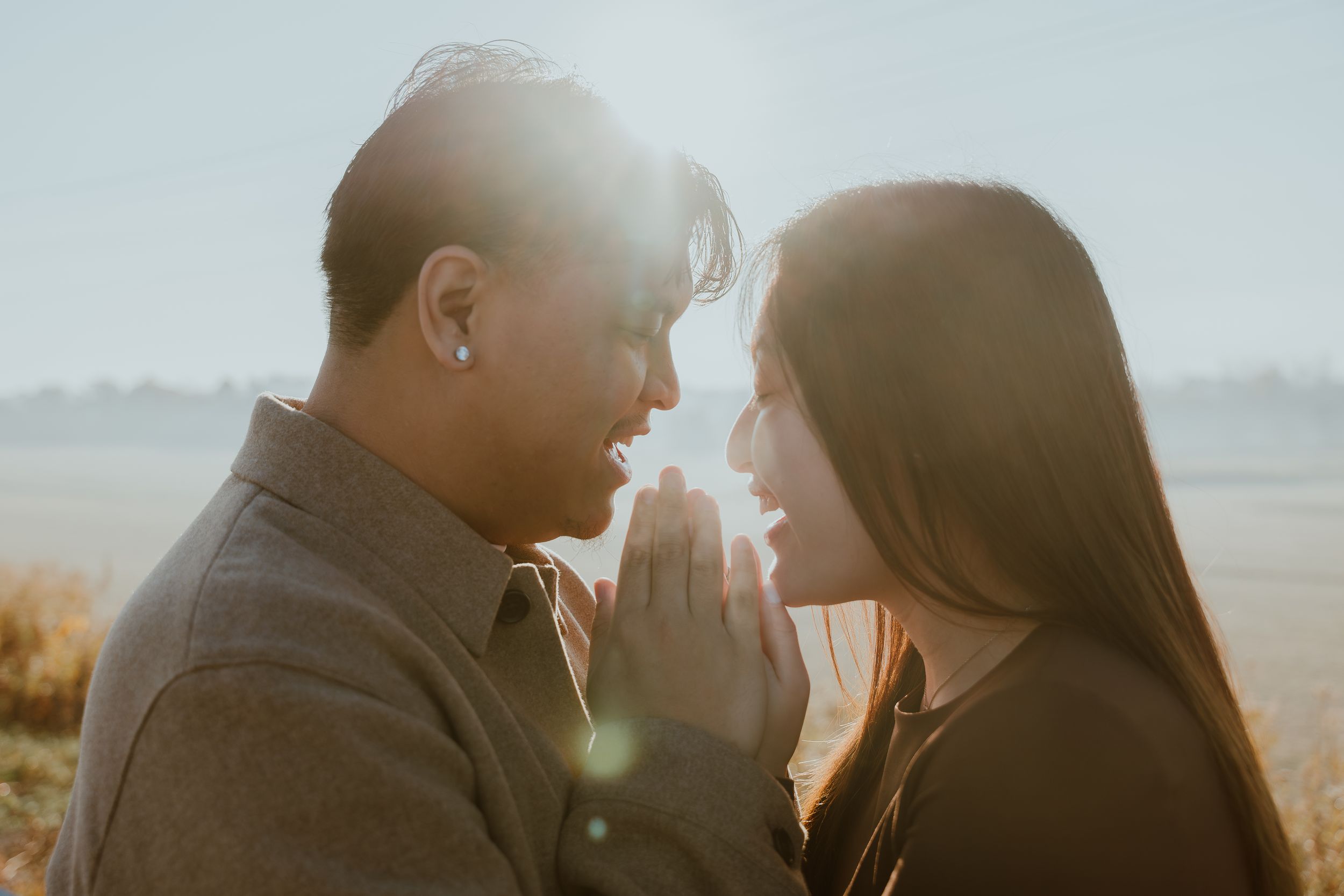 Intimate moment between a couple silhouetted against a sunlit rural landscape.