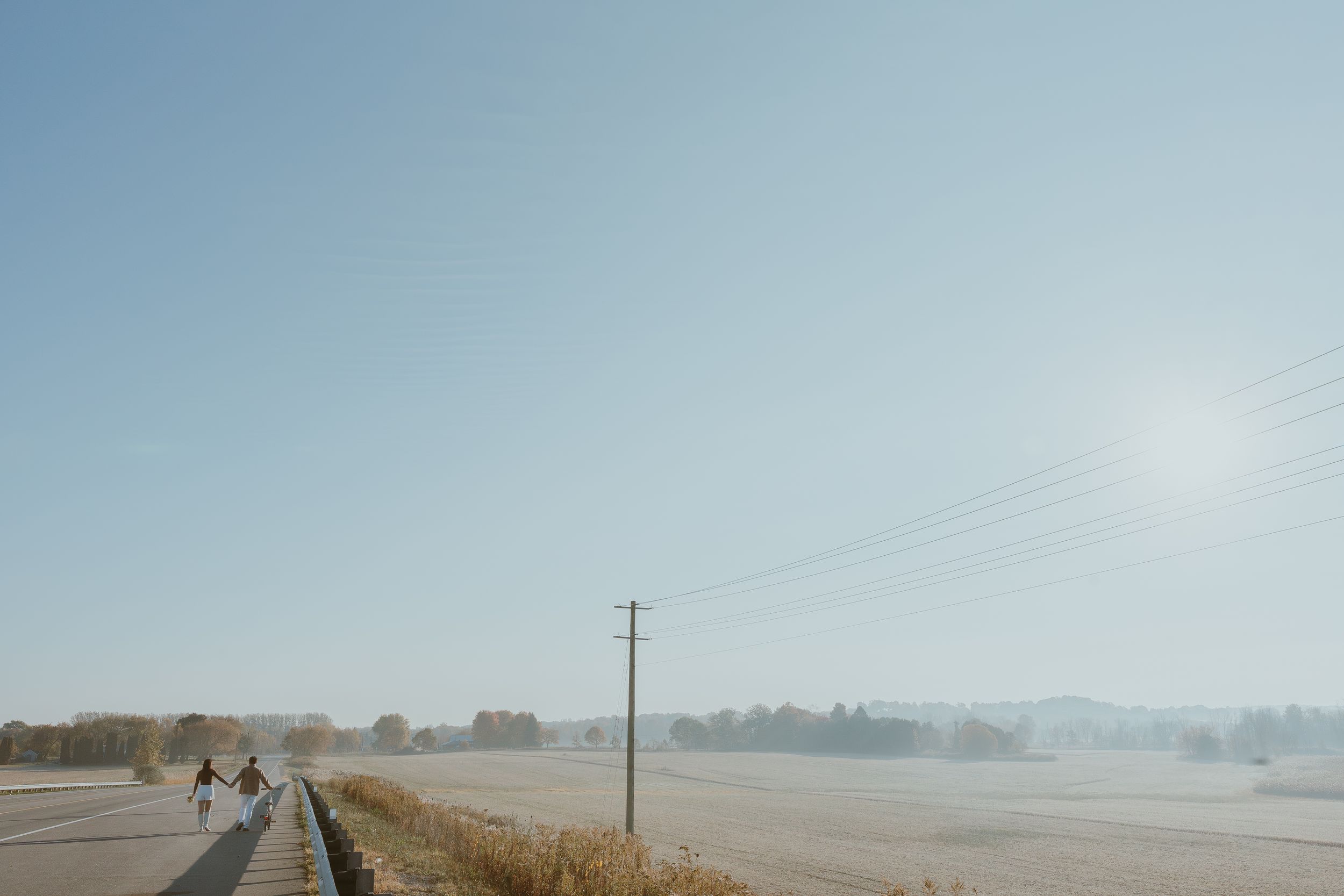Scenic rural landscape with power lines and distant cyclists on a foggy morning.