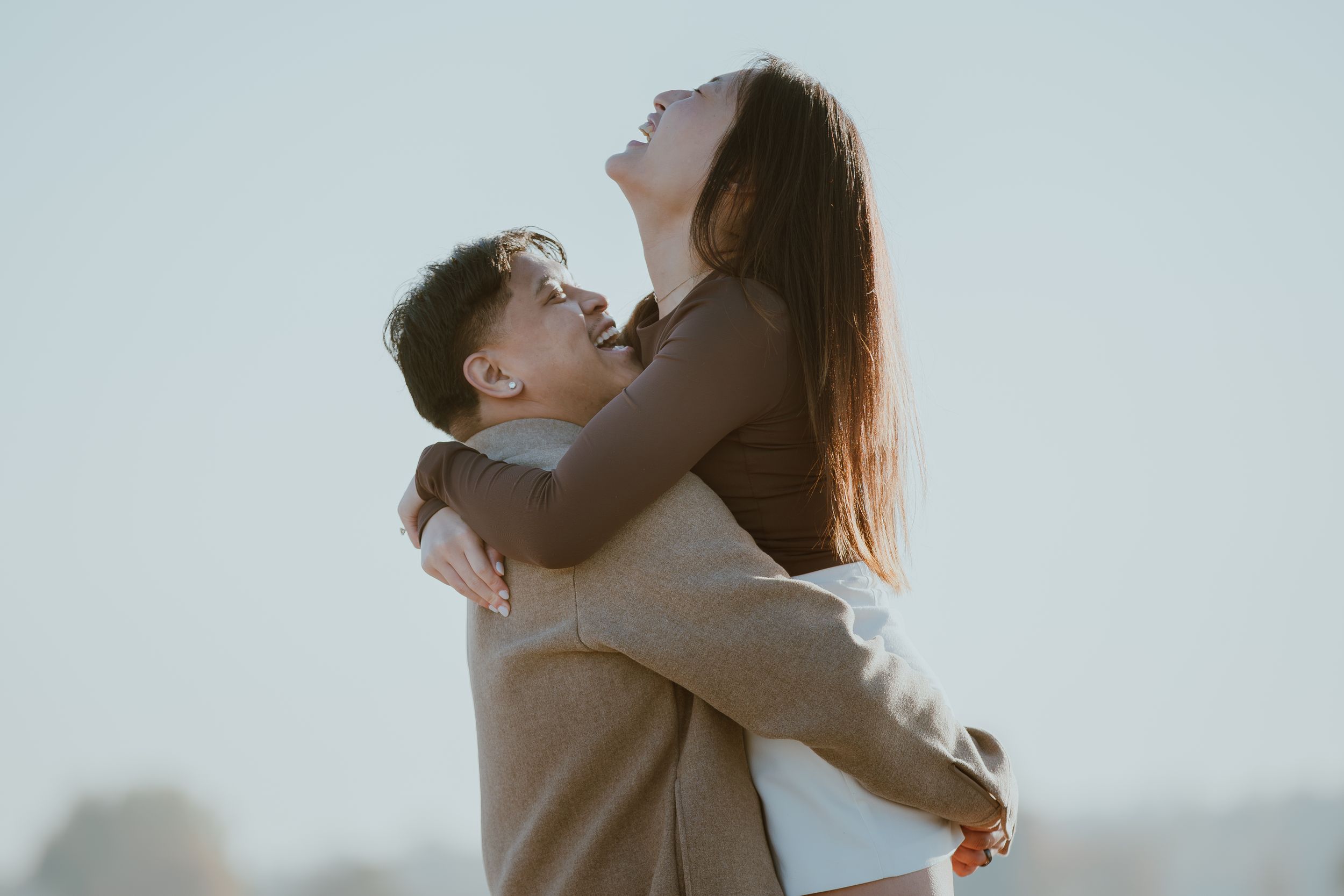 Joyful couple sharing an intimate embrace against a bright sky background.