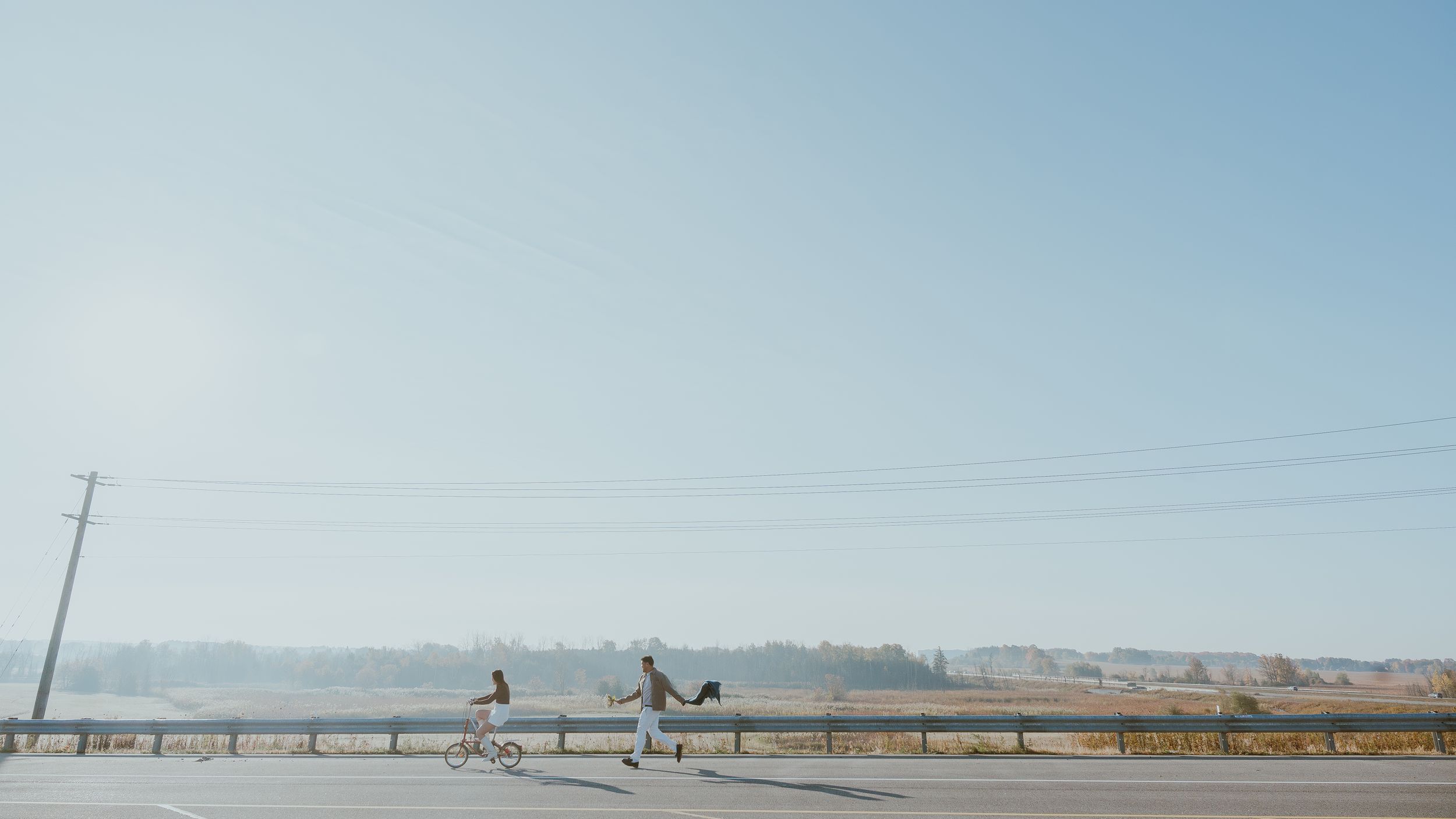 Cyclists on a rural road with power lines and mountains in the misty distance.