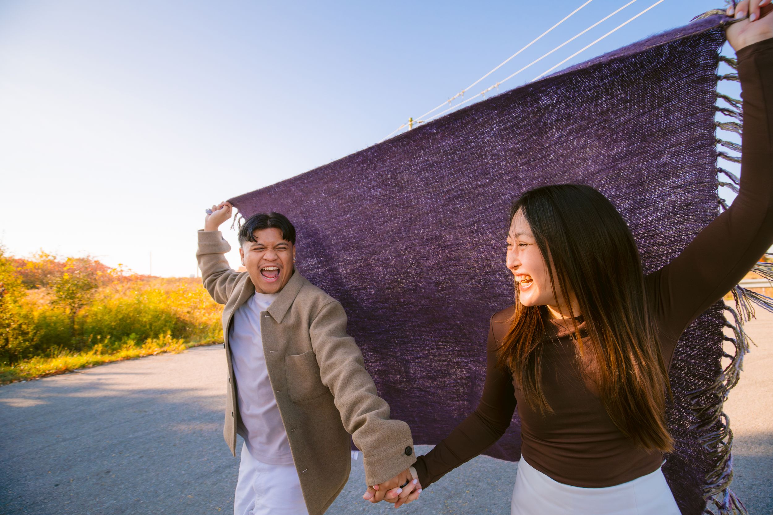 A couple playfully dances on a road with a brick wall and sunset in the background.
