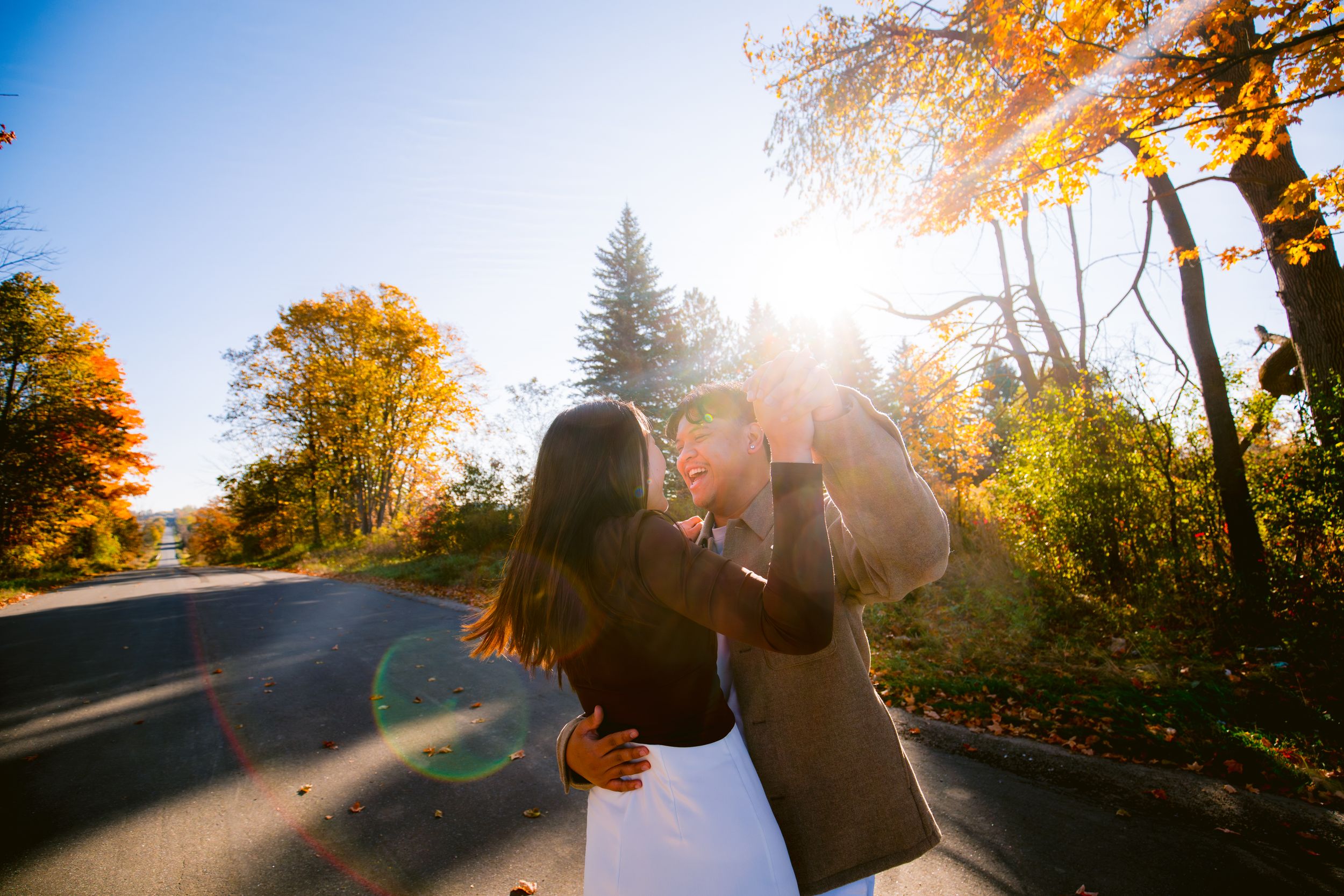 A couple shares a romantic moment on a sunlit autumn road with golden leaves overhead.