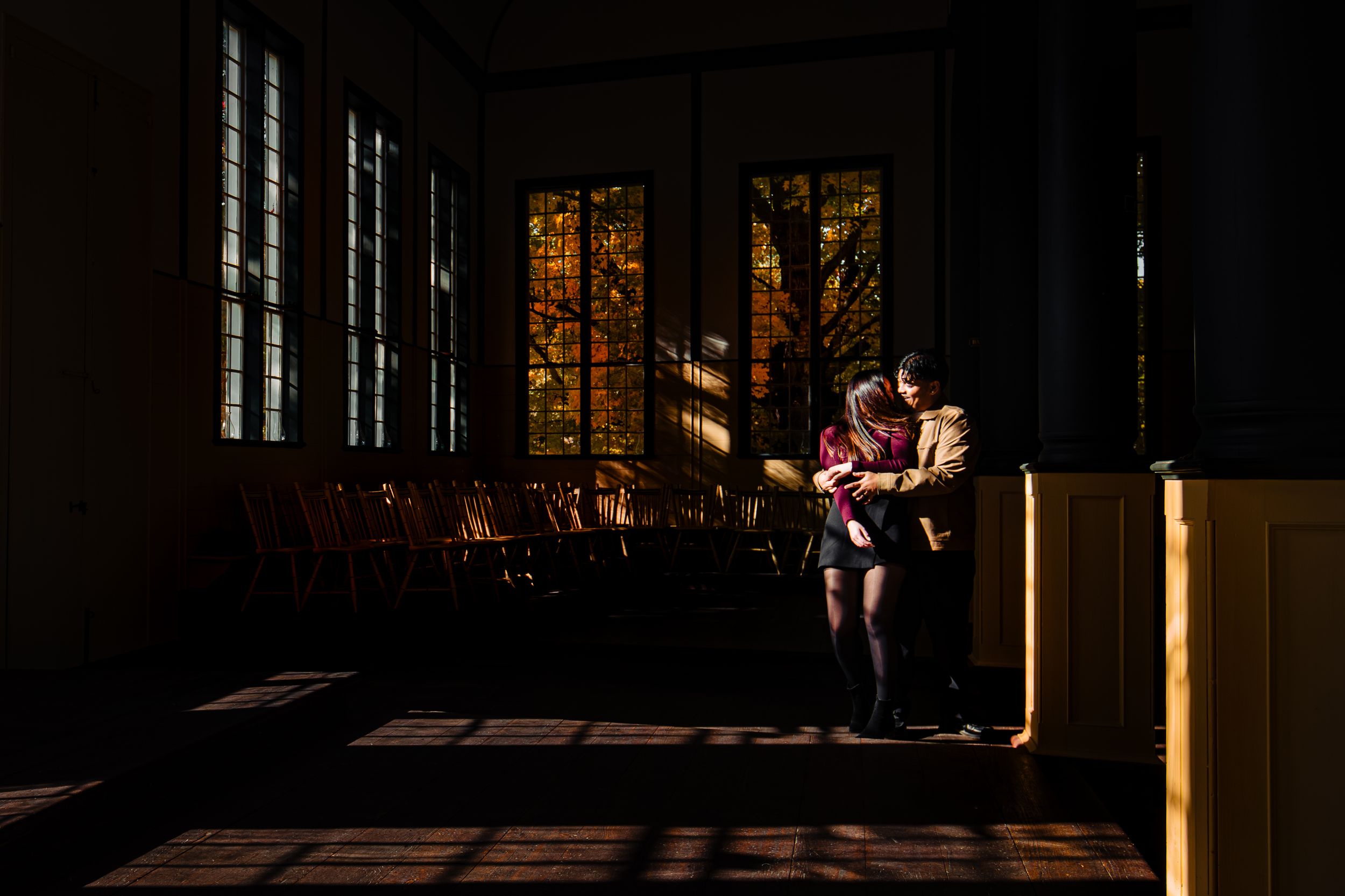Warm sunlight streams through windows onto a couple in a dimly lit interior space.