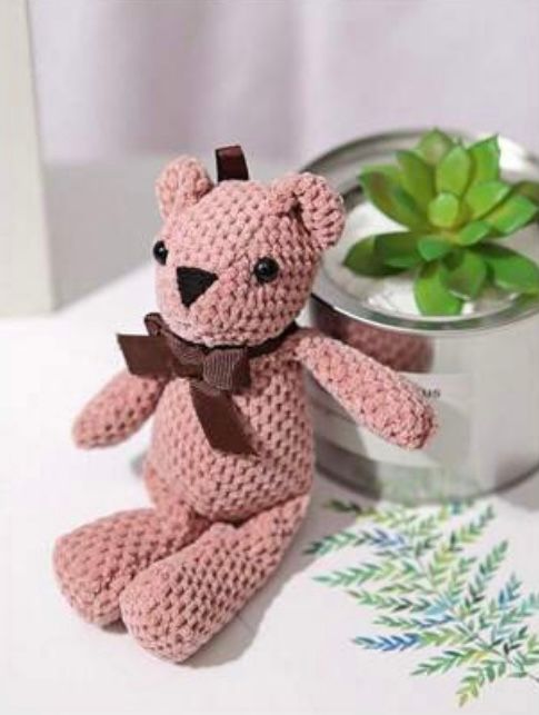Pink knitted teddy bear with brown bow tie next to succulent plant.