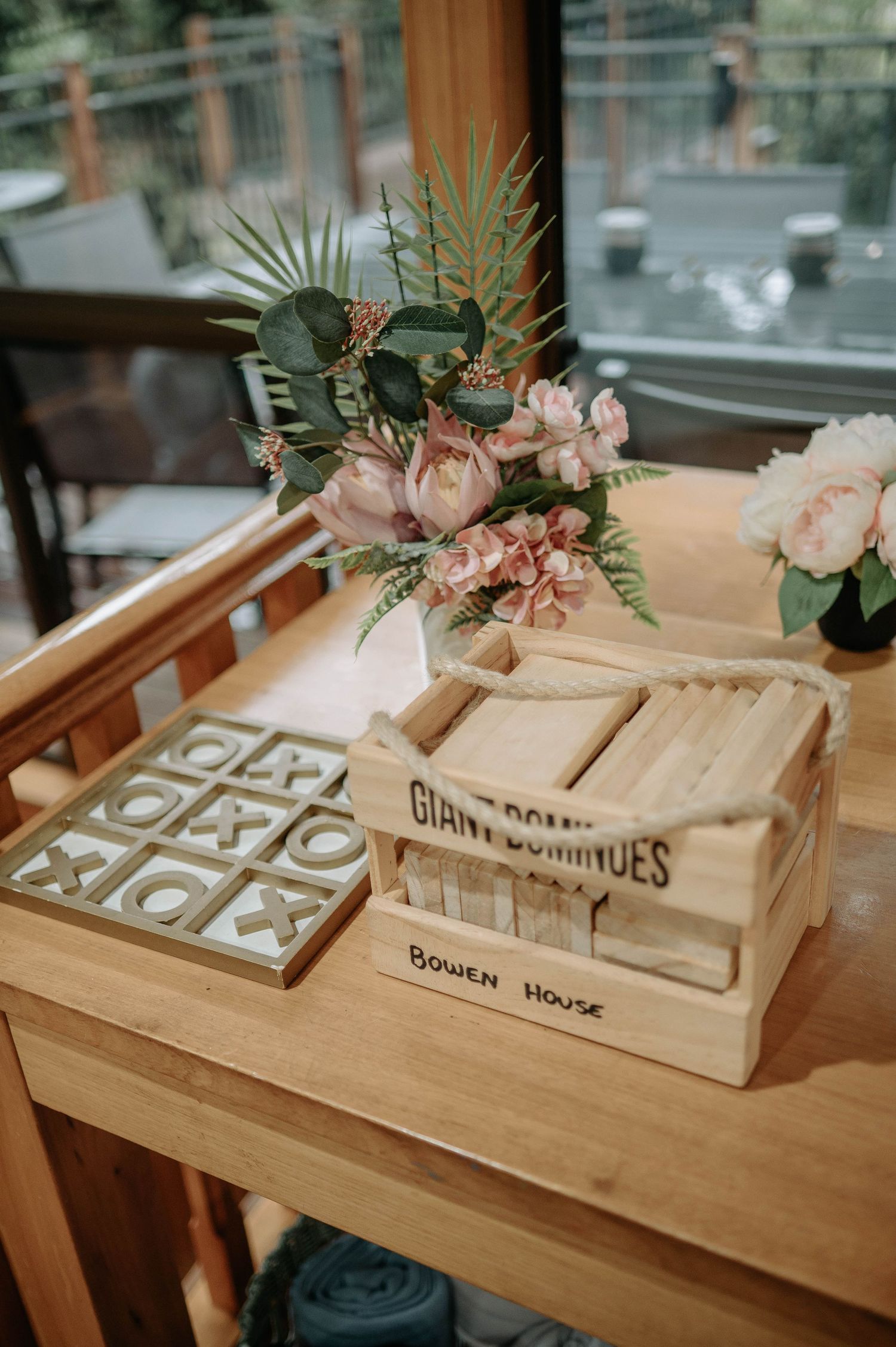 Wedding decor featuring tic-tac-toe game and wooden box with pink floral arrangements.