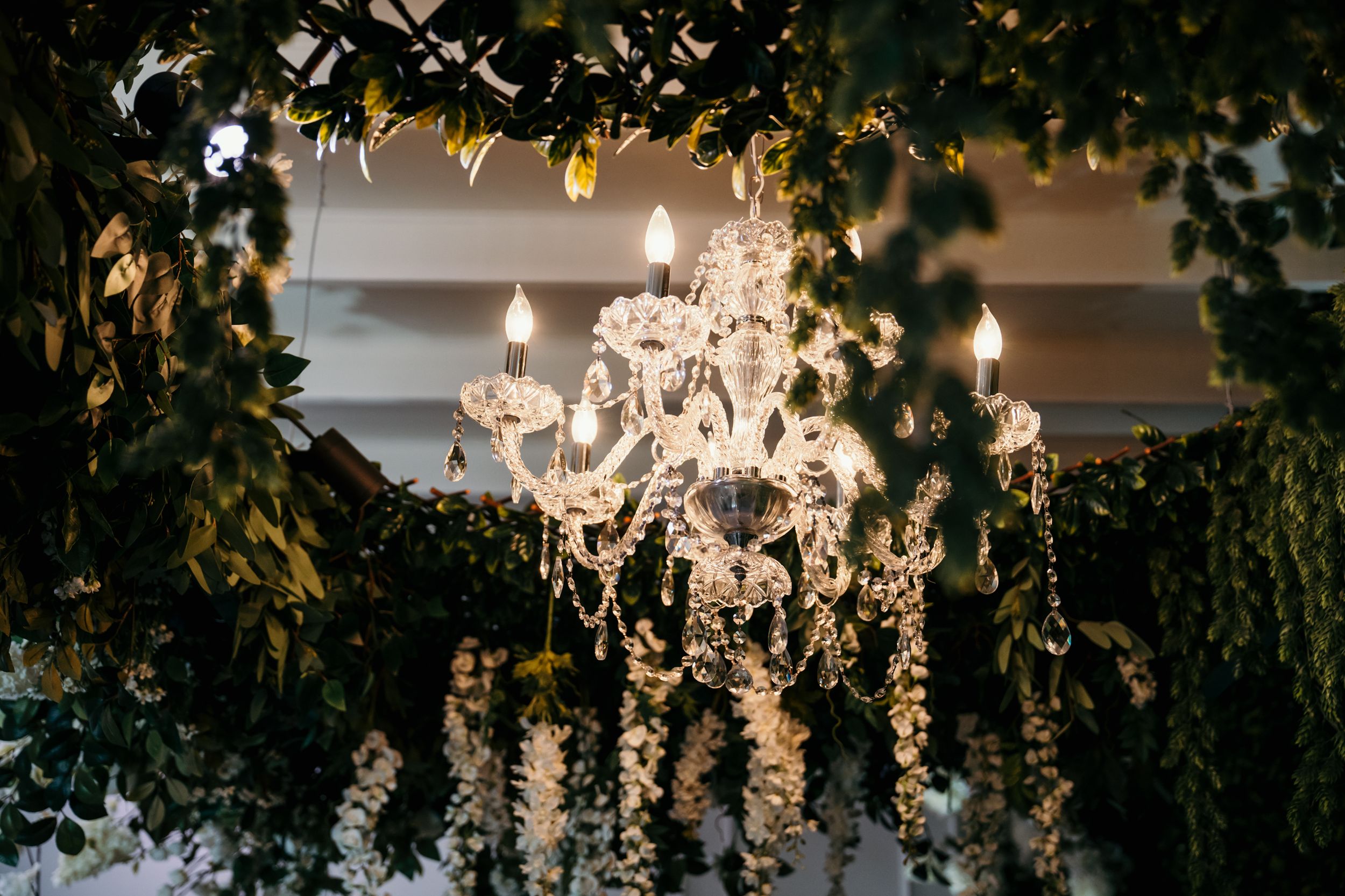 Elegant crystal chandelier glowing amid green foliage and fairy lights creating a romantic ambiance.