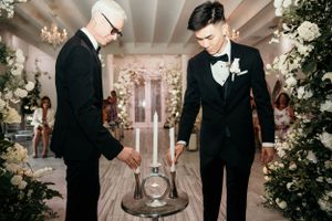 Two people performing a unity ceremony ritual with an hourglass at an indoor wedding reception.