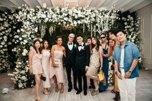 Wedding party poses together in front of luxurious white floral archway at reception venue.