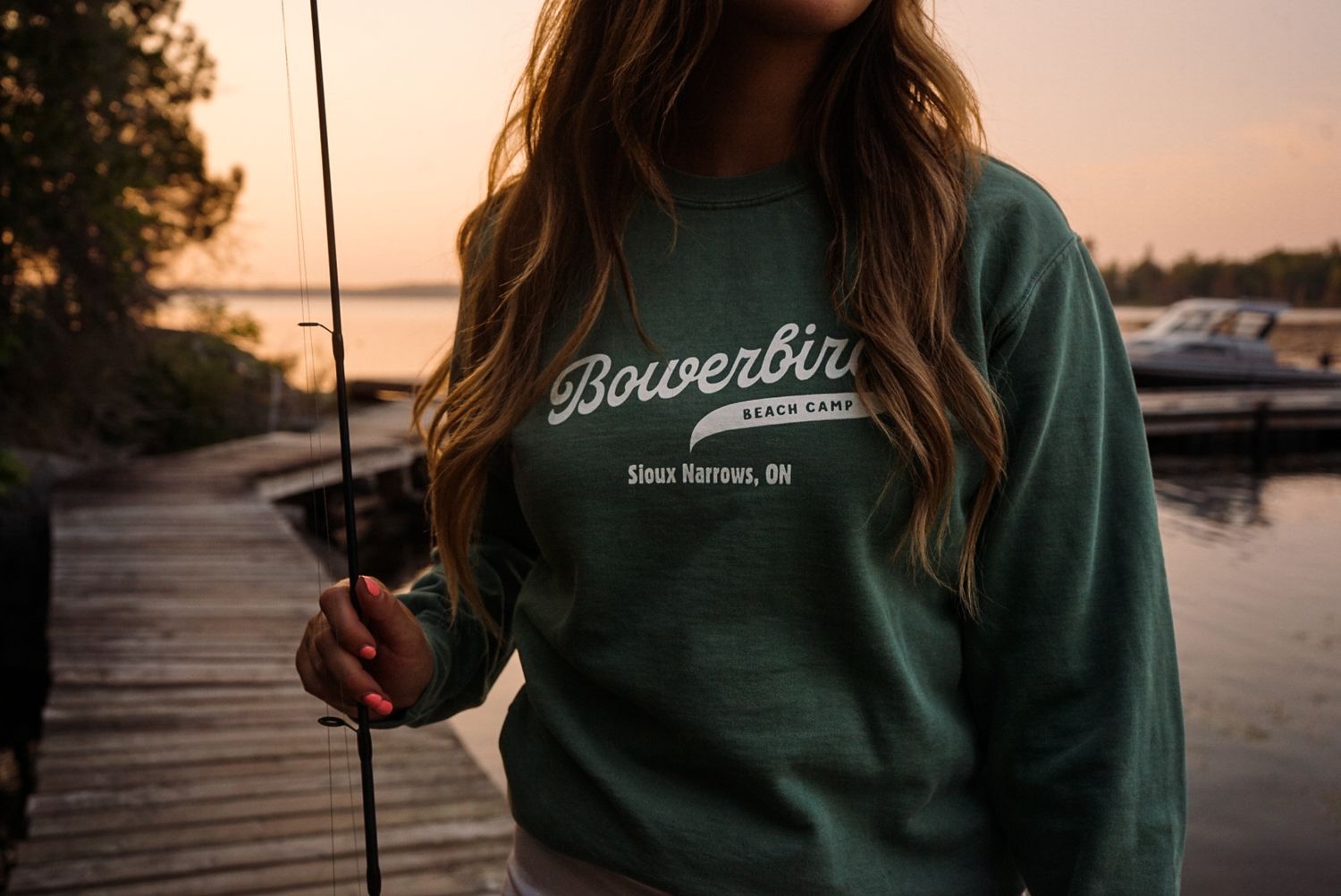 Person wearing green sweatshirt holding fishing rod during sunset at a lake.