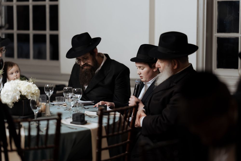 A group seated at a formal dining table with traditional black hats and attire.