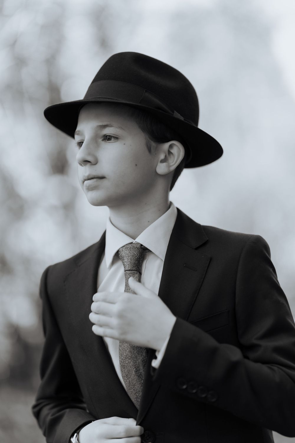 Classic portrait of someone in formal attire and fedora against blurred background.