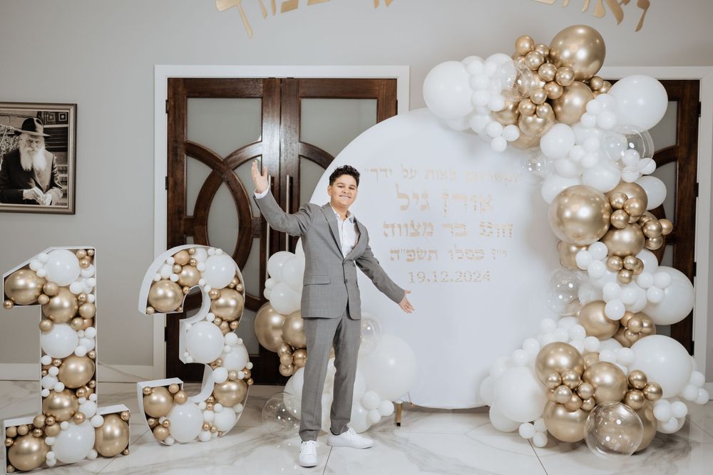 A celebratory backdrop with gold and white balloon arch and decorative signage.