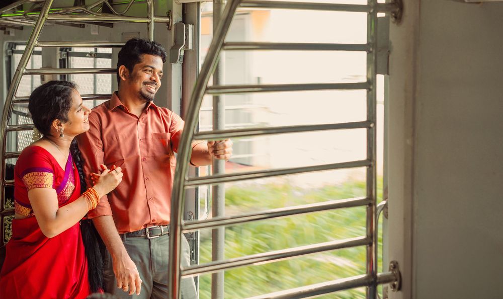 Two people standing by a window in a bright indoor setting, one wearing red and another in salmon colored attire.