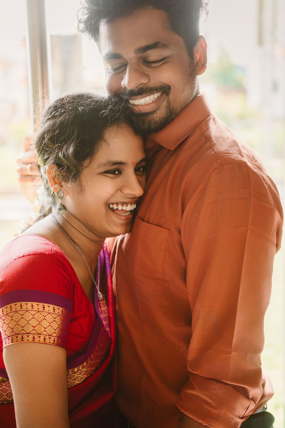 A couple wearing traditional Indian attire share a joyful moment together while embracing and smiling warmly.