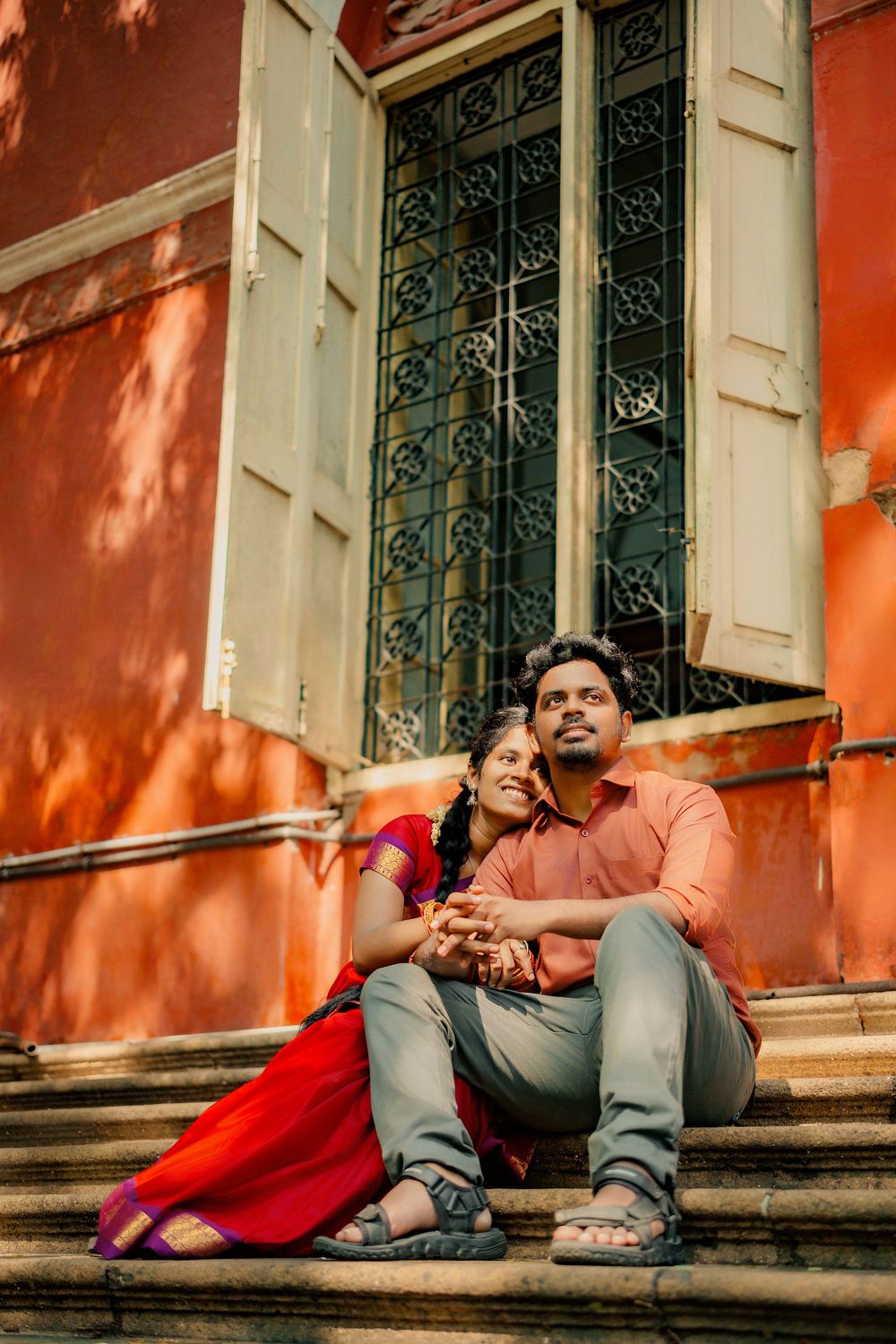 Couple in traditional Indian attire sit close together on red-painted stone steps.
