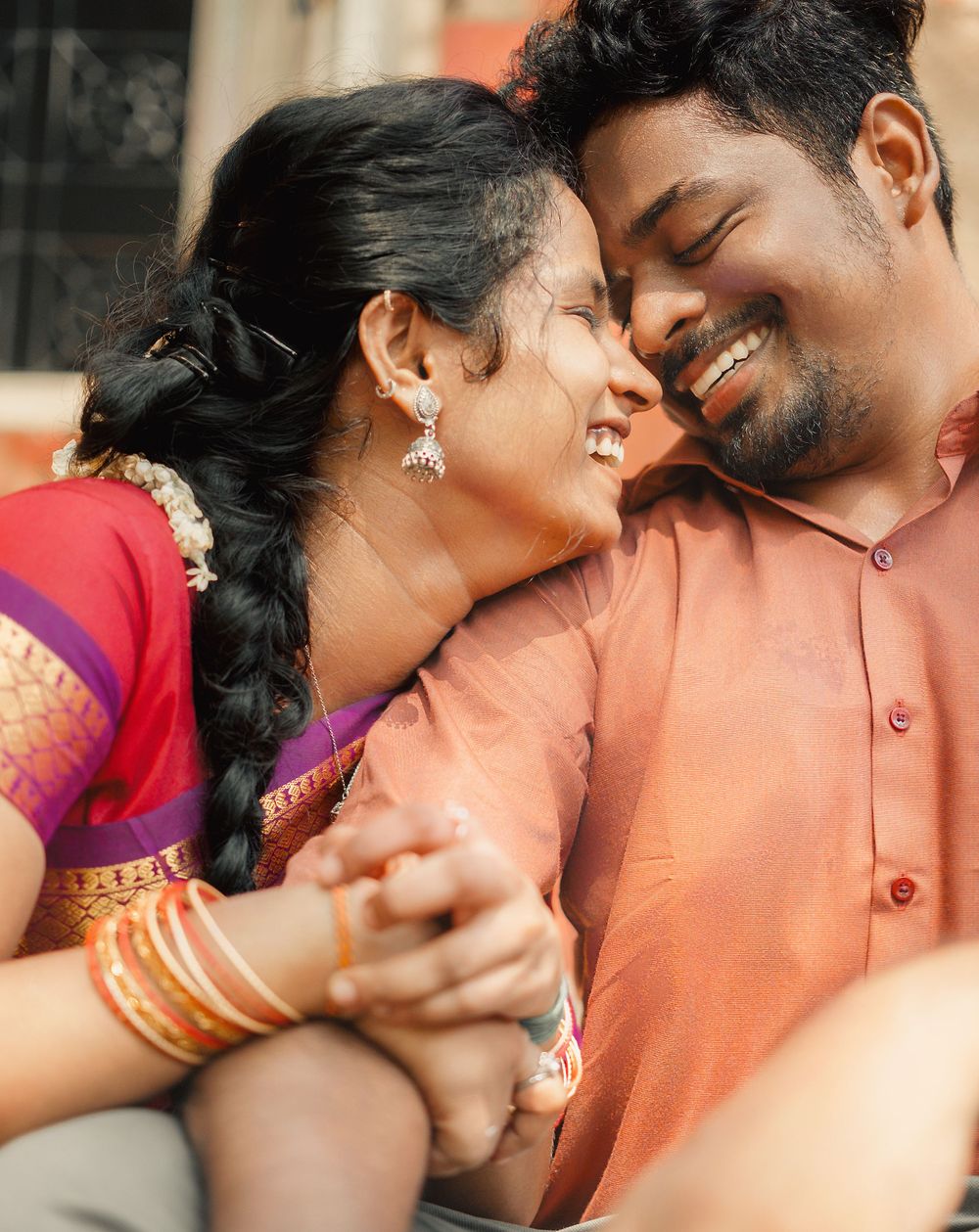 A couple shares an intimate moment together, wearing traditional South Asian attire in warm tones.
