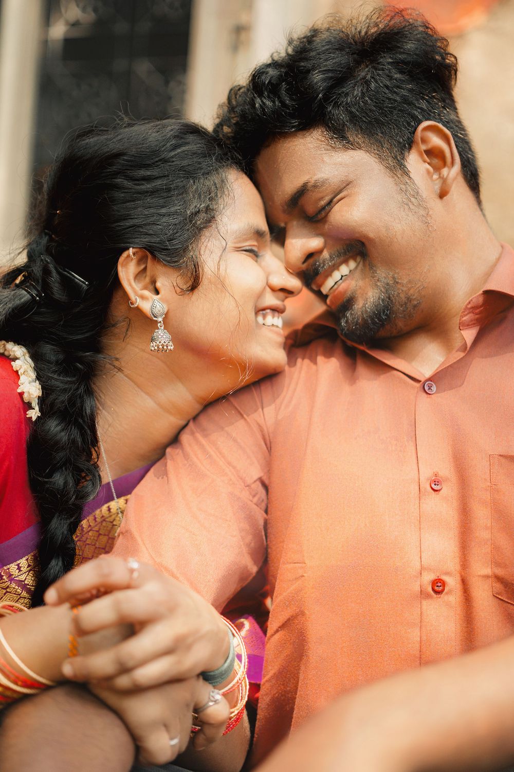 A loving couple in traditional Indian attire share an intimate moment while holding hands and smiling.