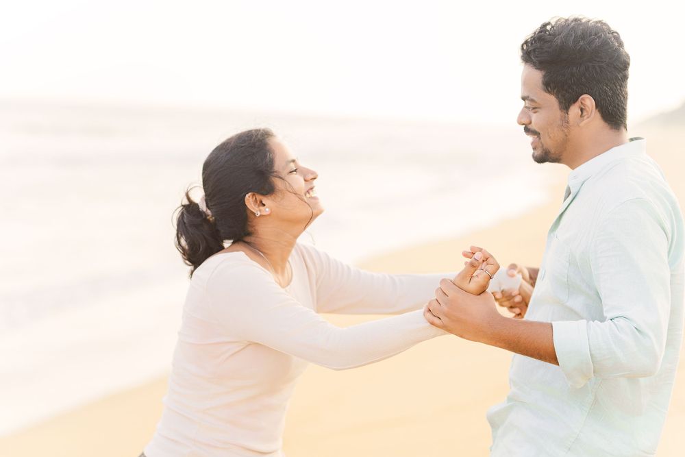A couple holds hands and laughs together on a misty beach during sunset.
