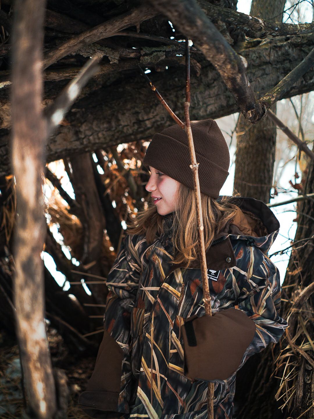 Hunter in camouflage gear standing among tree branches during autumn season.