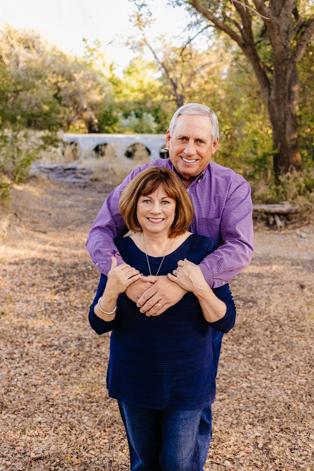 Mature couple embraces outdoors on an autumn day with natural scenery in the background.