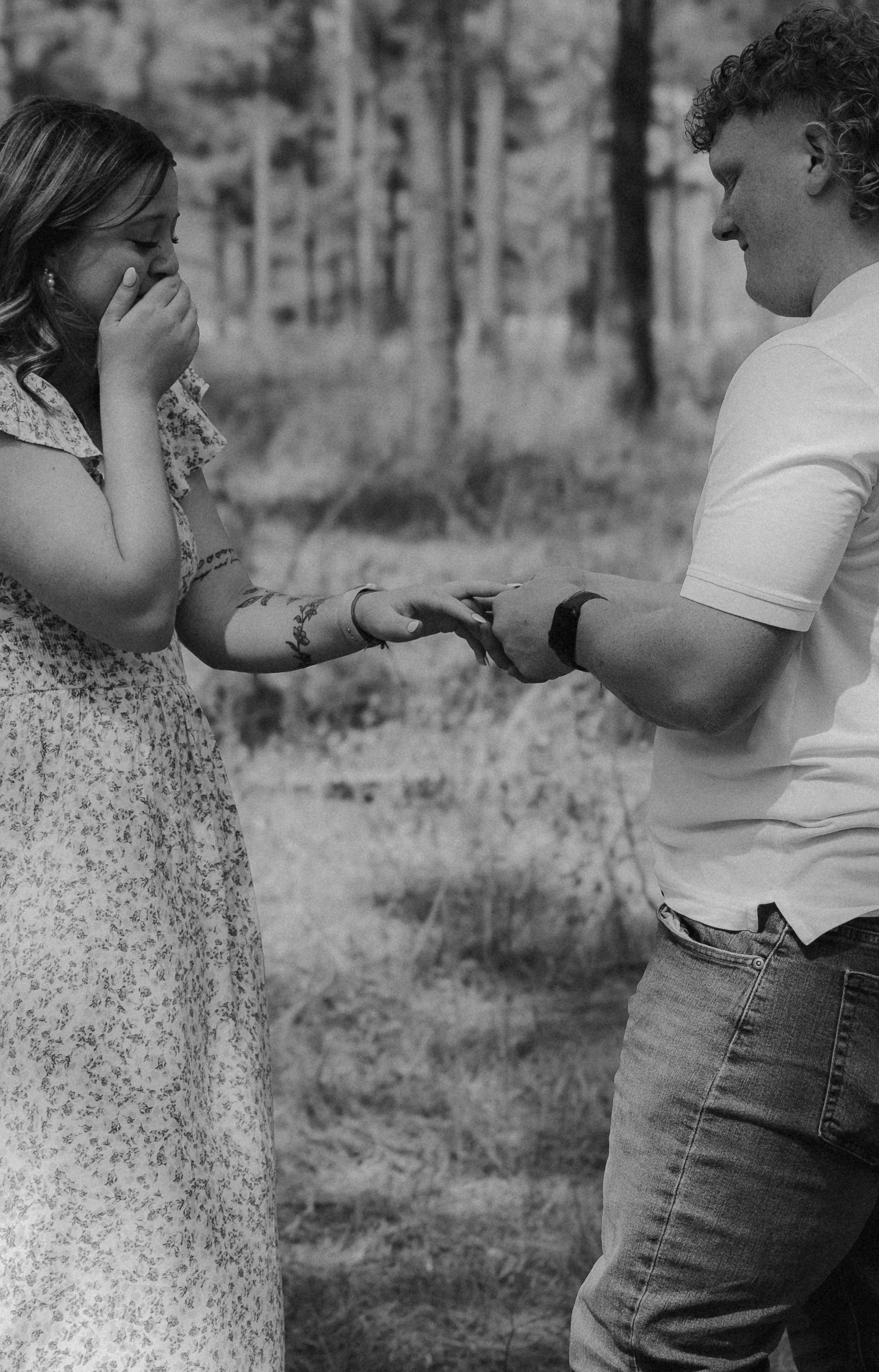 A couple shares an emotional moment during a proposal in a forest setting.
