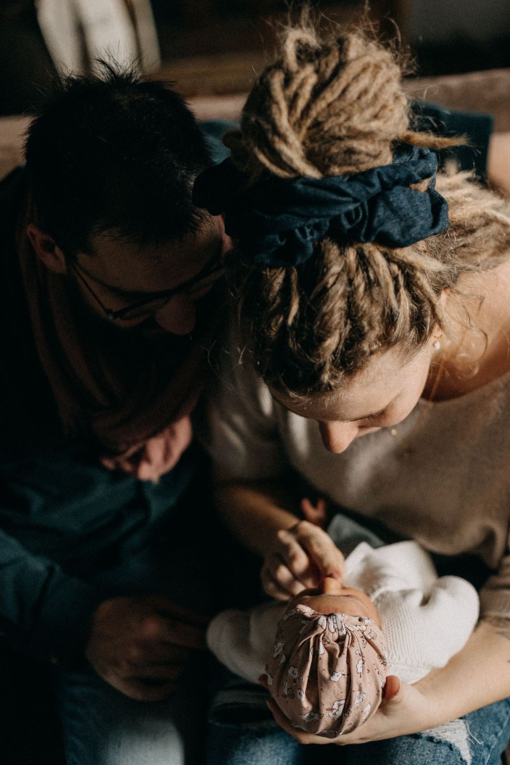 Parents lovingly cradling their sleeping newborn while sitting together on the couch.