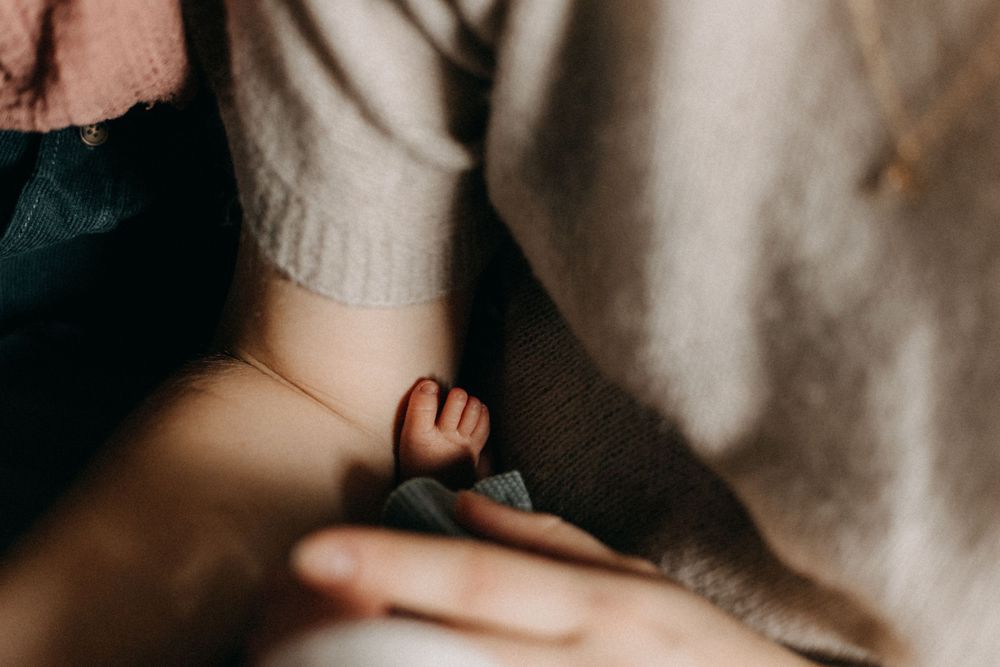 Intimate detail shot of a tiny baby hand reaching out against a soft fabric background.