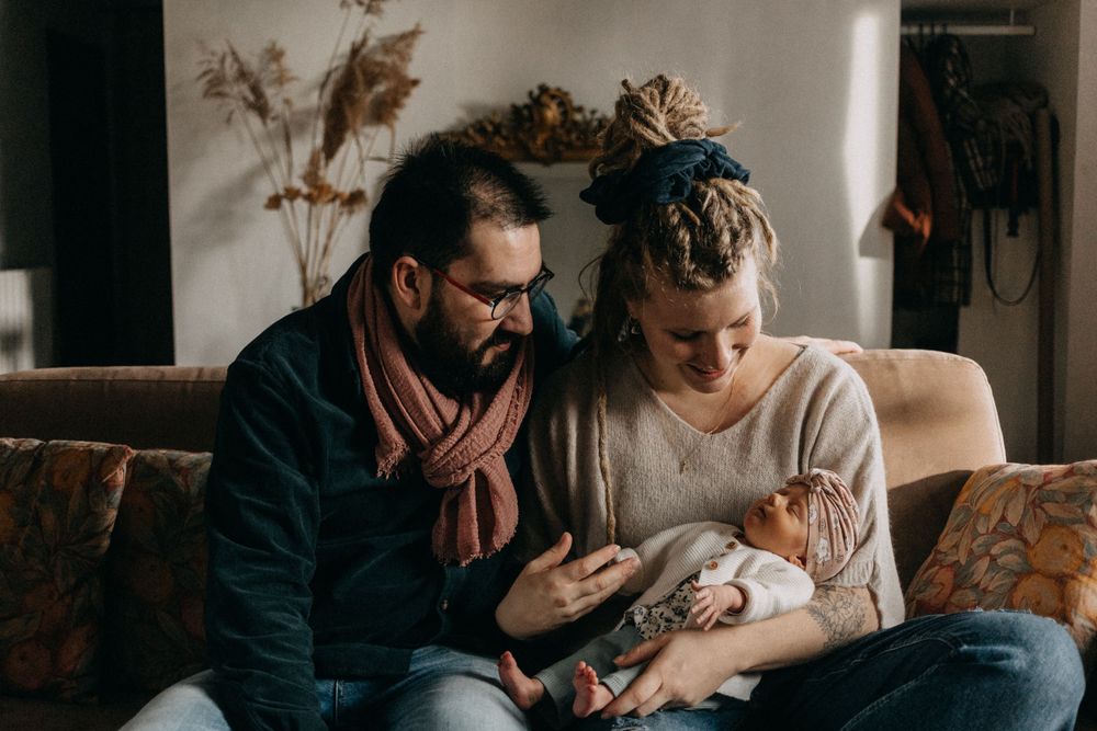 A couple sits on a floral couch holding and gazing at their newborn baby in an intimate family moment.