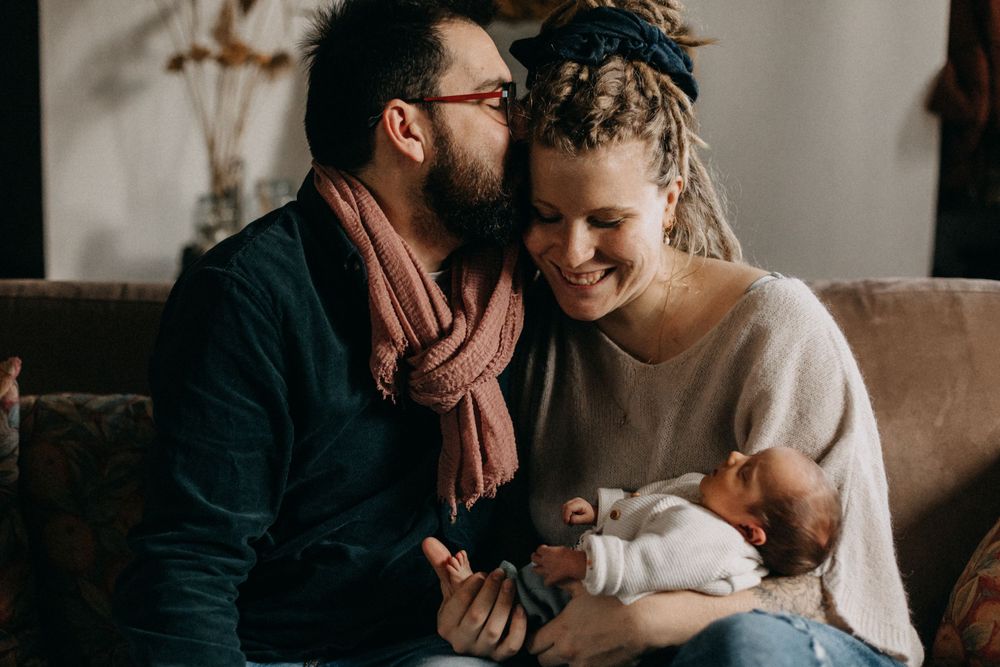 Intimate family moment shared on a brown couch as parents lovingly gaze at their newborn.