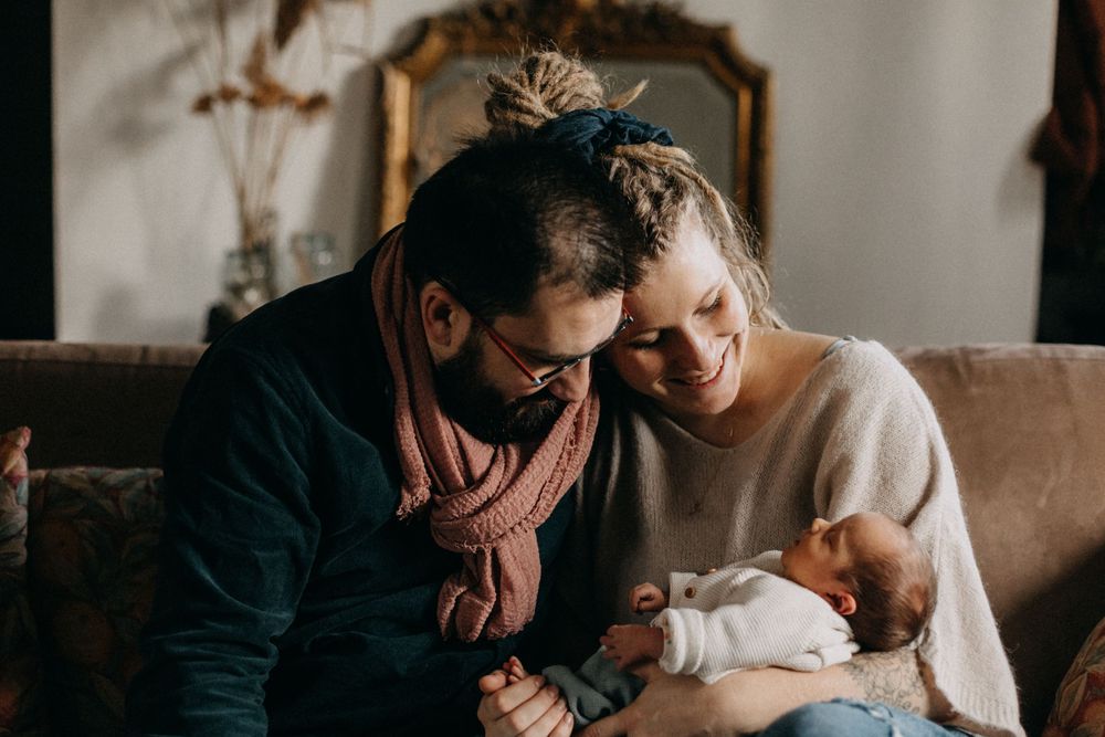 Parents sharing a tender moment with their newborn baby on a vintage brown sofa.