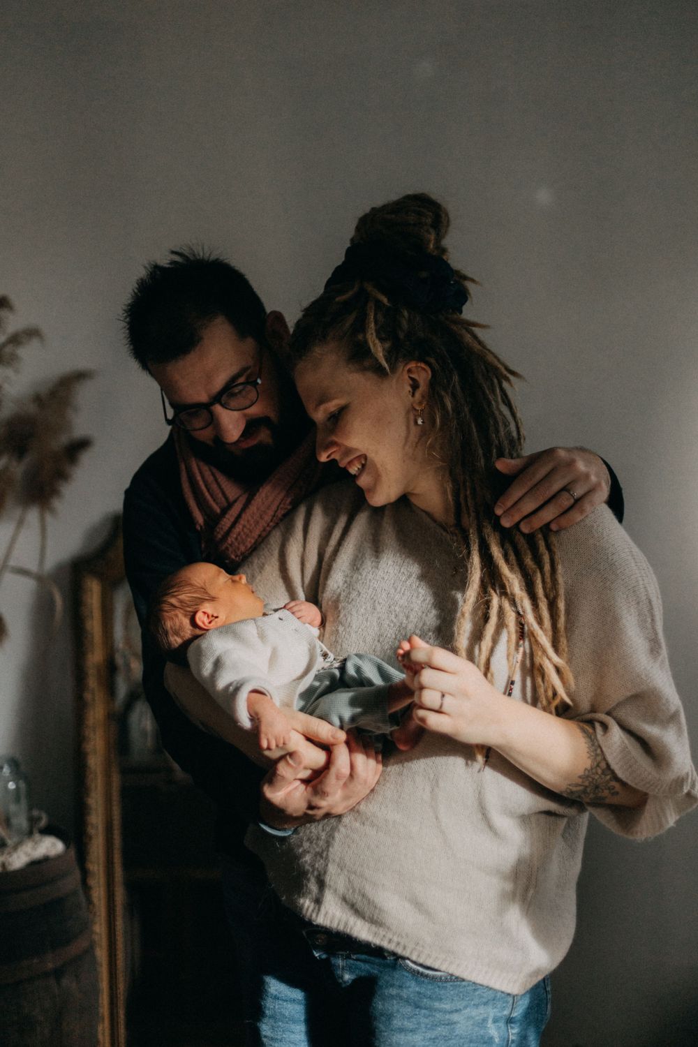A joyful moment between parents as they hold their newborn baby among dried flowers and natural decor.