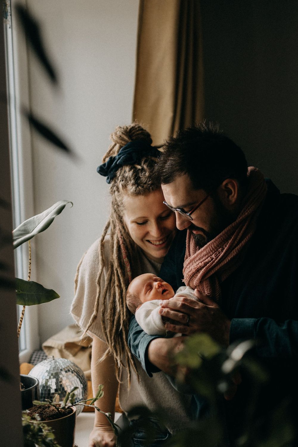 Intimate family moment by window with newborn baby in natural light.