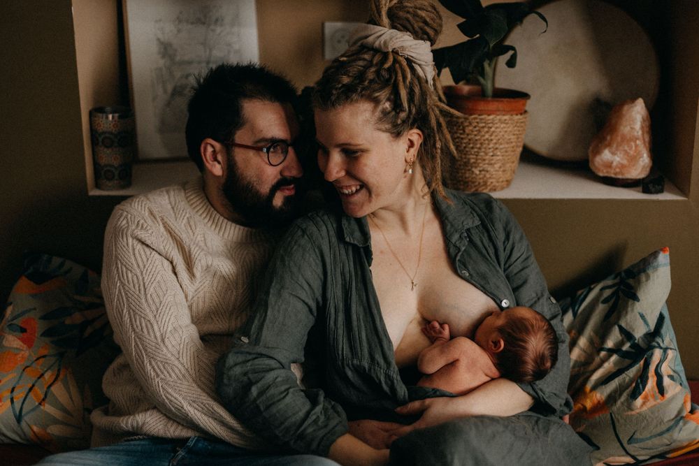 An intimate family moment showing new parents cuddling with their newborn baby on a couch.
