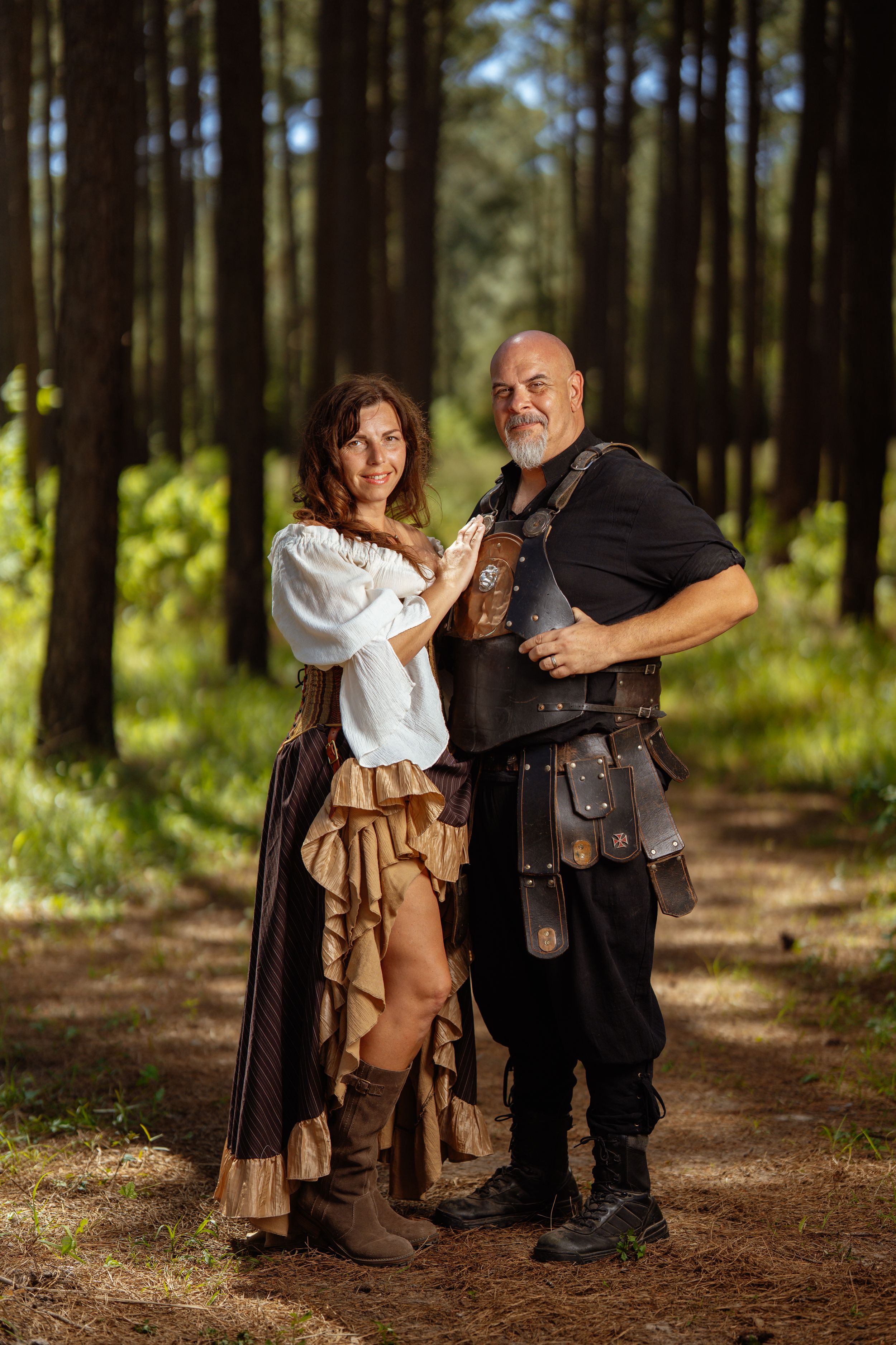 People dressed in medieval renaissance costume with leather accessories pose together on a forest path in dappled sunlight.