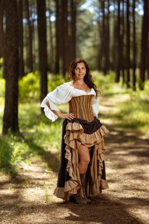 Medieval-inspired fantasy costume with corset and ruffled skirt photographed on a sunlit forest path.