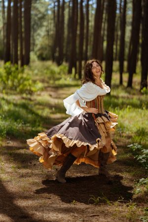A flowing brown and white renaissance dress swirls dramatically during a dance movement in a forest setting.