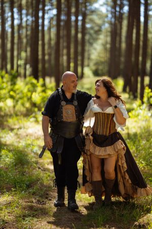 A costumed couple shares a joyful moment while walking along a sunlit forest trail.