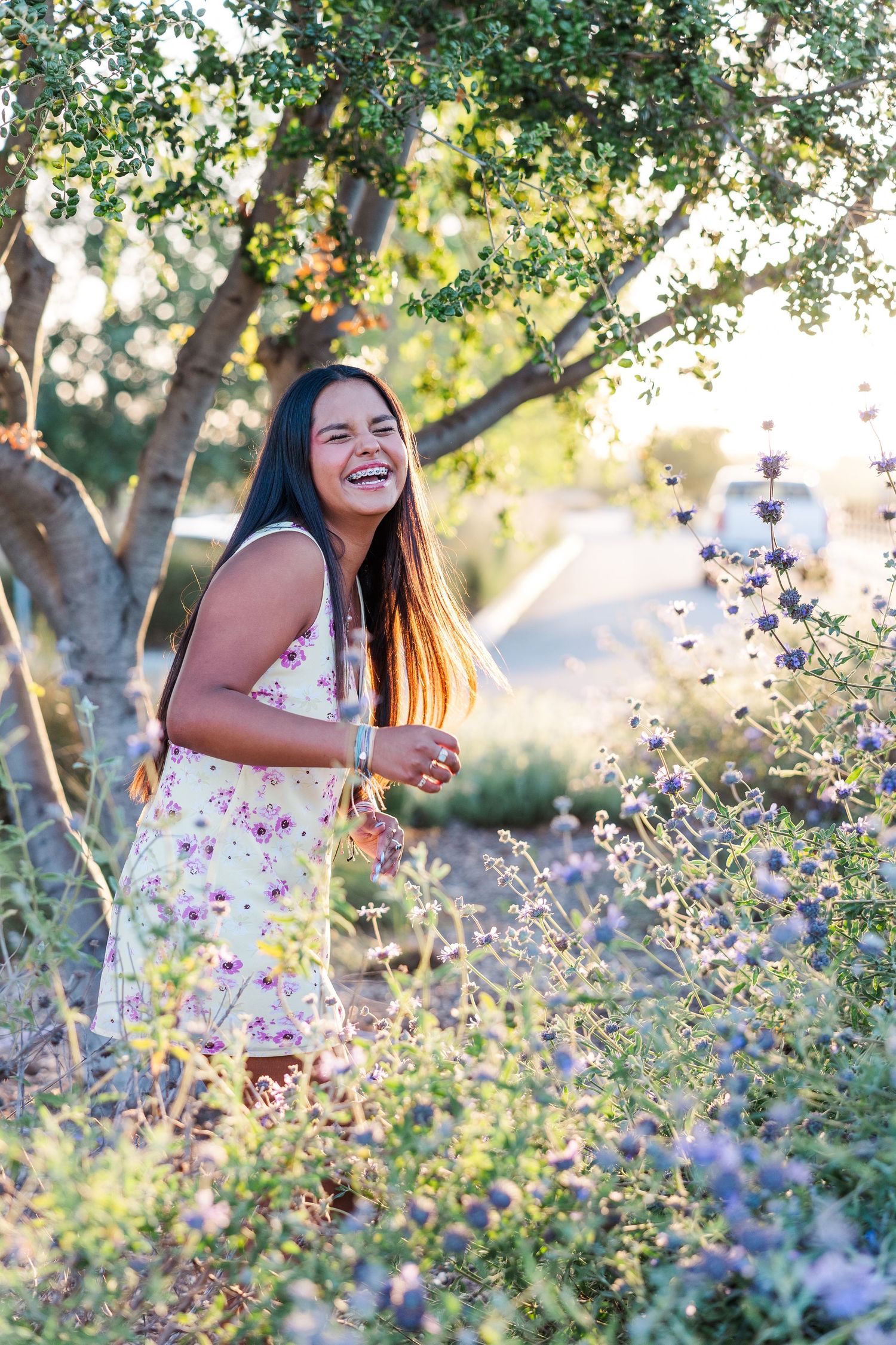 Joyful person wearing a floral dress laughs while standing among blooming wildflowers and trees on a sunny day in Simi Valley CA