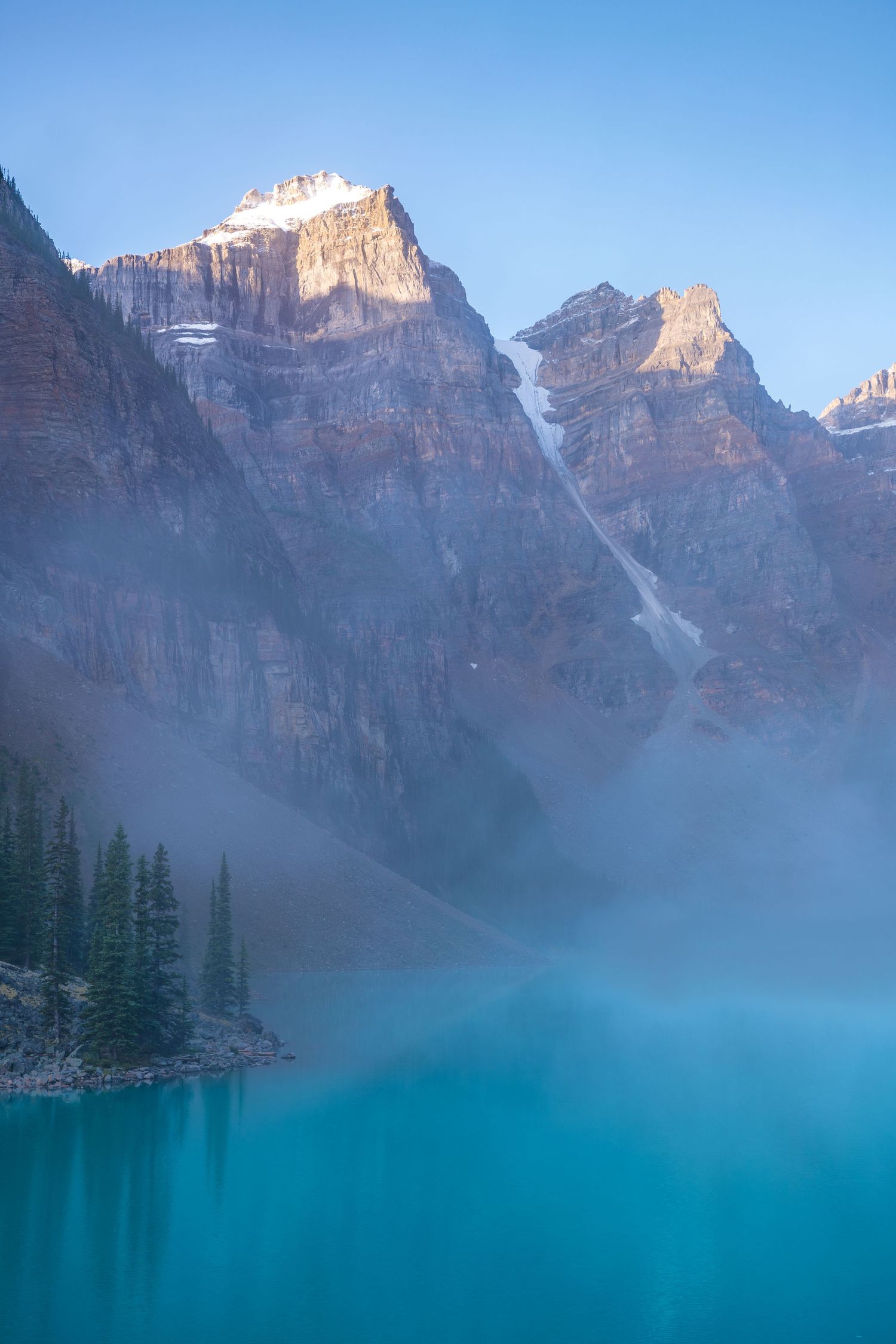 Misty morning at Moraine Lake with towering mountain peaks and vibrant turquoise waters.