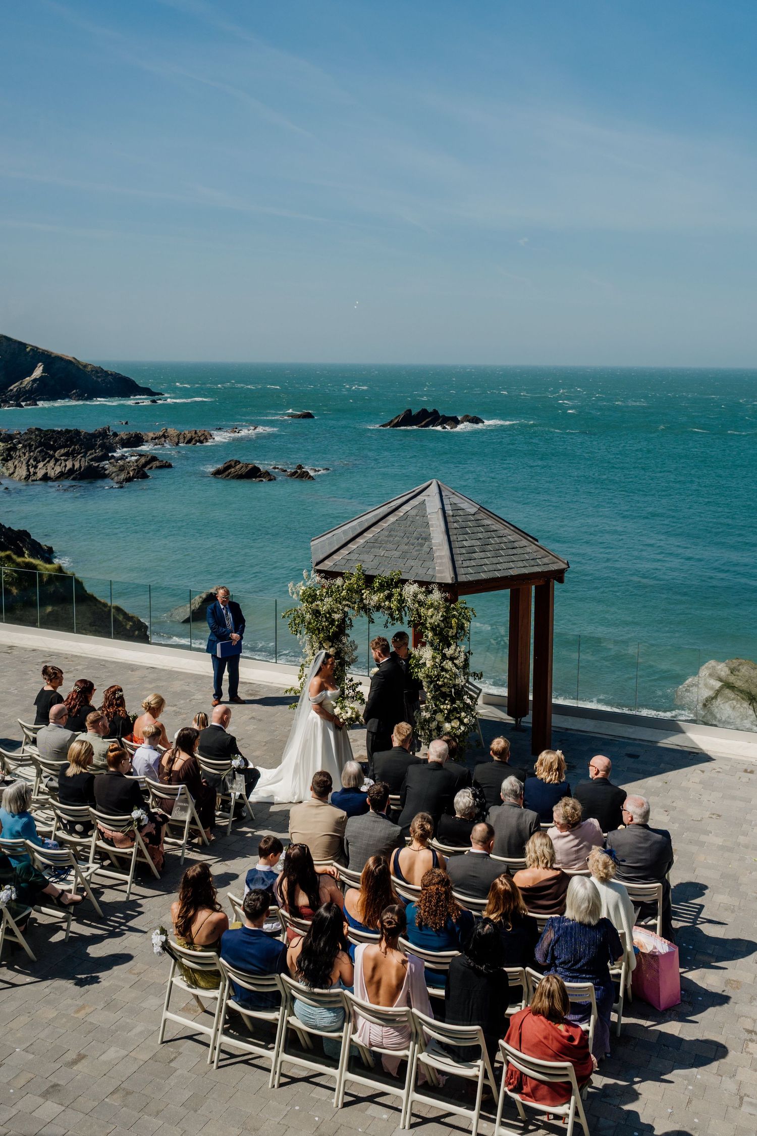 Outdoor wedding ceremony at tunnels beaches overlooking turquoise ocean waters, with guests seated facing couple at floral arch.