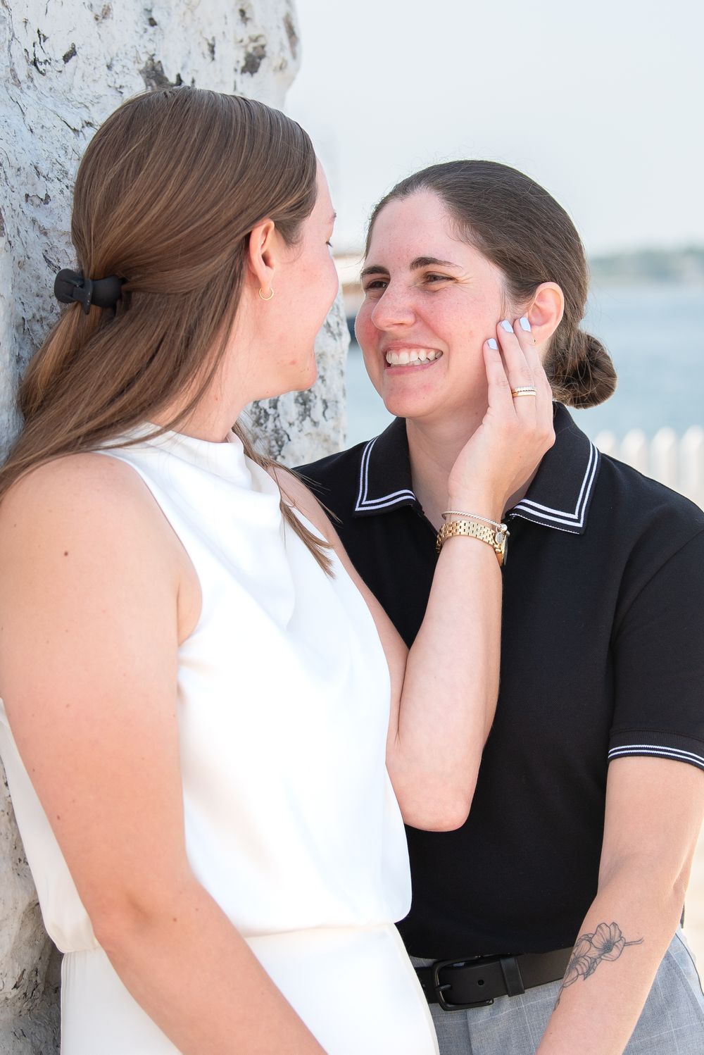 A couple in black and white attire shares tender moments in a seaside photoshoot.