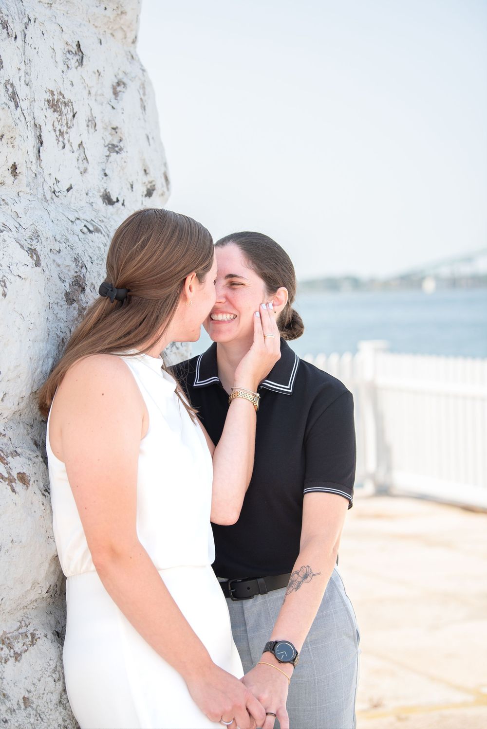 A couple shares an emotional moment by a white pillar with the ocean in the background.