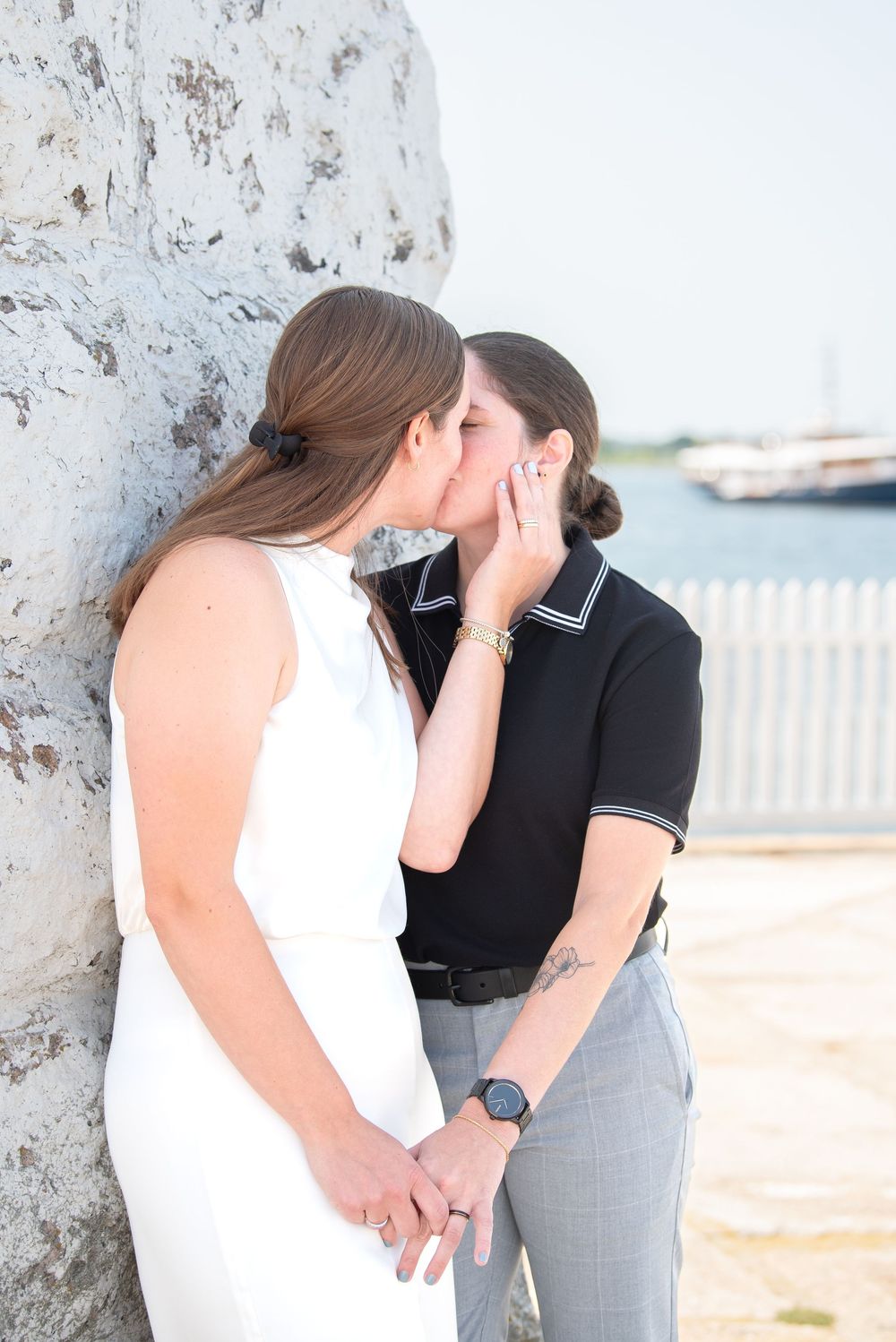 A tender moment shared between two people in contrasting outfits by a coastal wall.