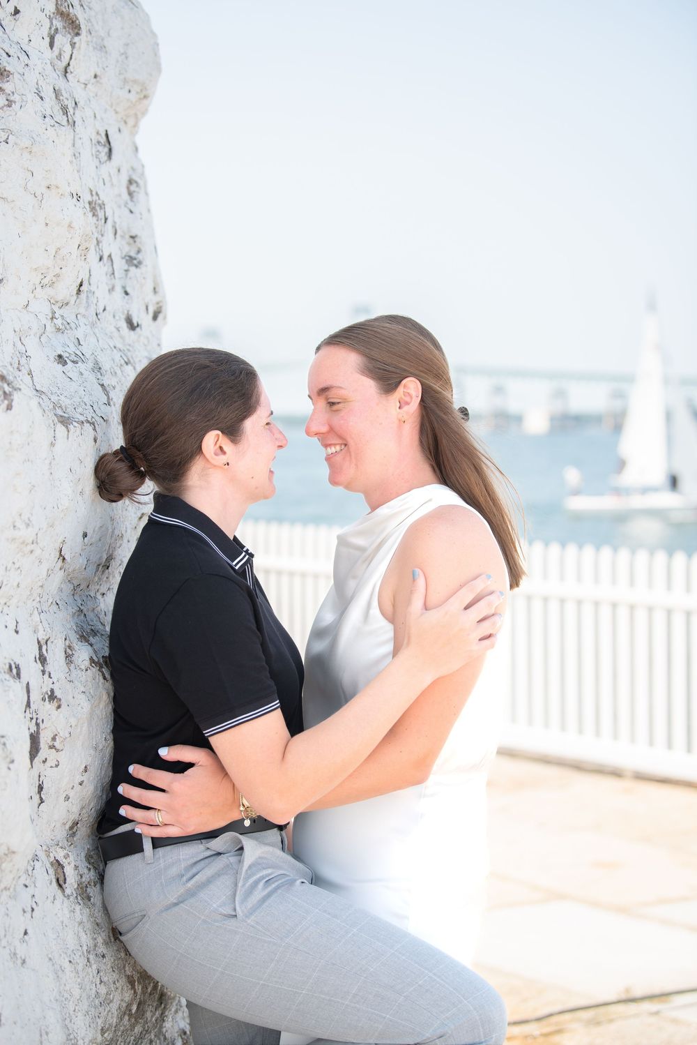 A romantic moment captured between two people against a white wall with a harbor view.