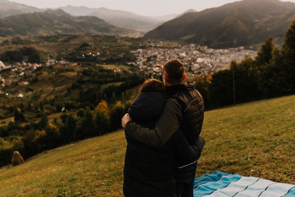 Couple embracing from behind while overlooking a picturesque mountain valley town at sunset.