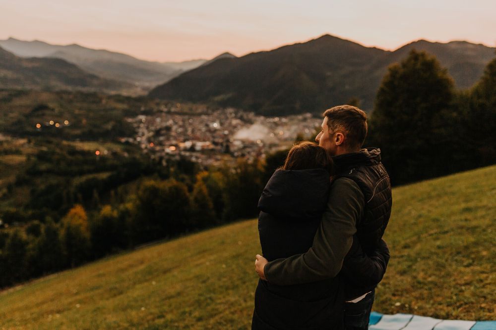 Couple embracing while overlooking a scenic mountain valley town at sunset.